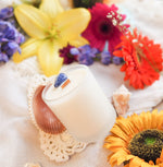 Crystal Candle with Sodalite stone and wooden wick, in frosted white glass vessel. Colorful flowers background