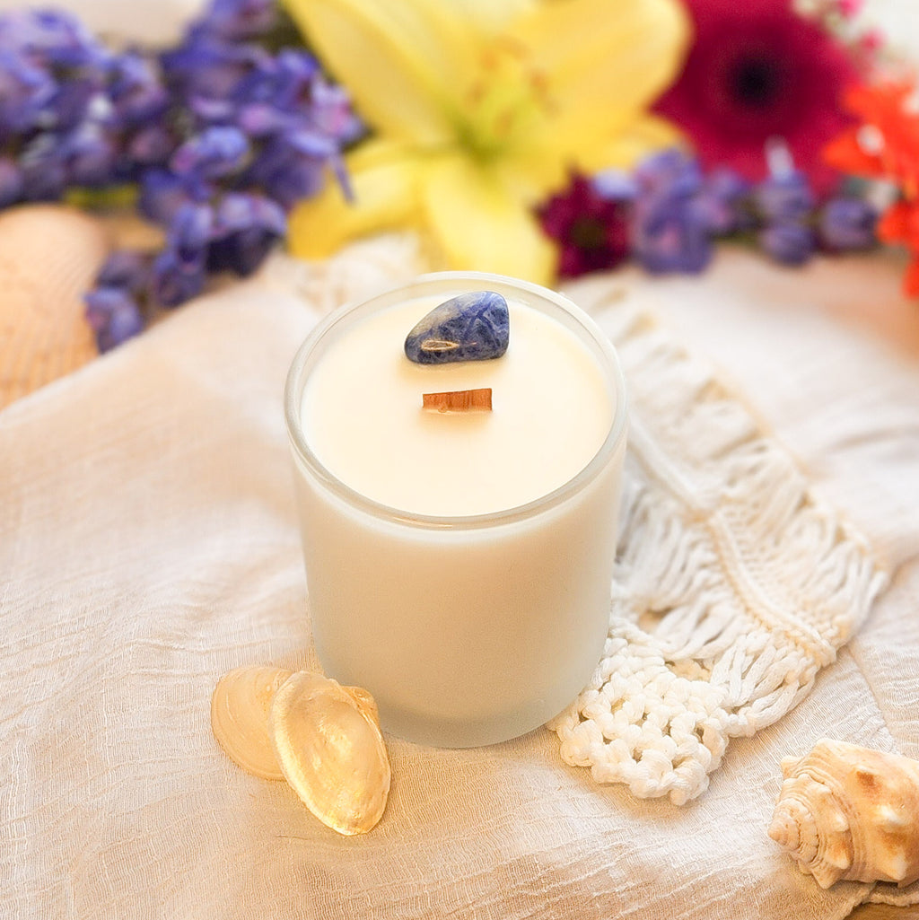 Crystal Candle with Sodalite stone and wooden wick, in frosted white glass vessel. Colorful flowers background